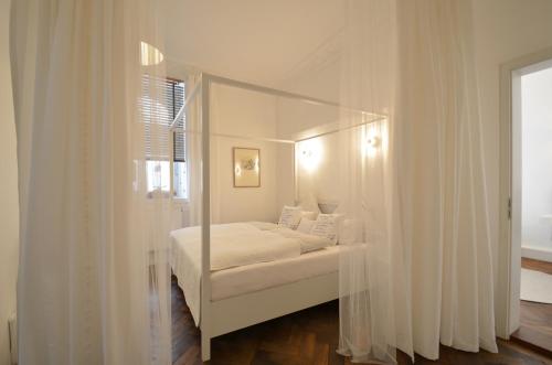 ミュンヘンにあるAsante-Design-Apartment Deluxe - very centralのベッドルーム(白いカーテン付きの天蓋付きベッド1台付)