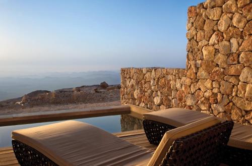 a patio with two chairs and a stone wall at Beresheet by Isrotel Exclusive in Mitzpe Ramon