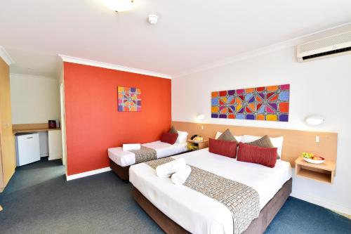 a hotel room with two beds and an orange wall at Diplomat Hotel Alice Springs in Alice Springs