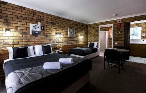 1 Schlafzimmer mit 2 Betten und Ziegelwand in der Unterkunft Park House Motor Inn in Oakey