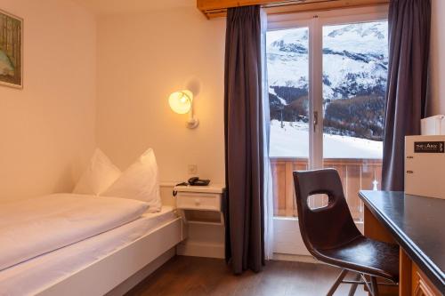 a bedroom with a bed and a desk and a window at Hotel THE LARIX ski-in ski-out in Saas-Fee