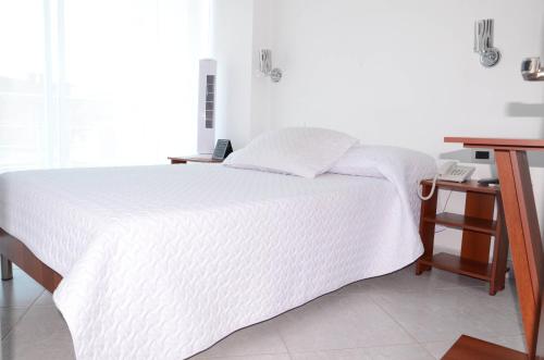 a bedroom with a white bed and a wooden table at Hotel Manhattan Barbosa in Barbosa