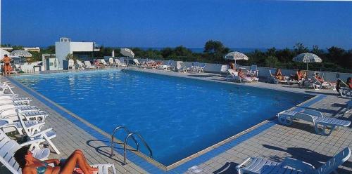 a large blue swimming pool with chairs and umbrellas at Apartment Pine Wood in Bibione