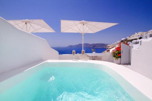 a swimming pool on the side of a house with umbrellas at Onar Villas - Onar Hotels Collection in Oia