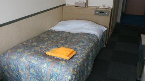 a bed with an orange towel on top of it at Business Hotel Motonakano in Tomakomai