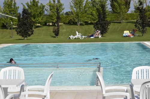 a swimming pool with white chairs and people in a park at Relais Corte Pontigliardo in Colà di Lazise