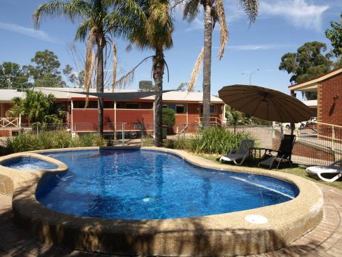 einem Pool mit einem Sonnenschirm vor einem Gebäude in der Unterkunft Old Coach Motor Inn Echuca in Echuca