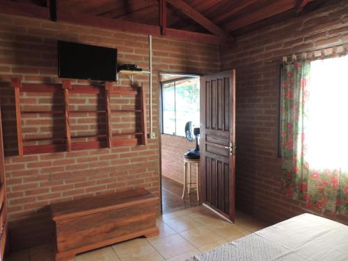 a room with a brick wall with a television and a door at Tocas do Lago in São Bento do Sapucaí