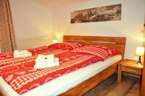 a bedroom with a large bed with red and white sheets at Tennladen Apartments in Niederau
