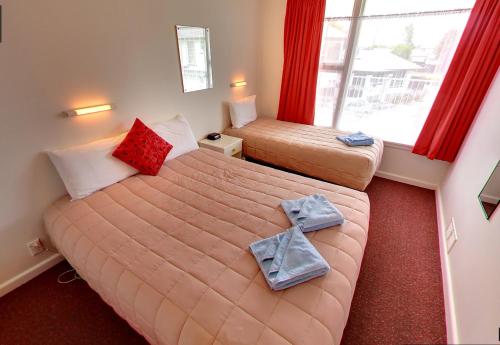 a bedroom with two beds and a window with red curtains at Belle Bonne Motel in Christchurch