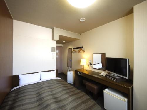 a hotel room with a bed and a desk with a television at Hotel Route-Inn Court Karuizawa in Miyota