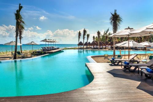 una piscina con sillas y sombrillas en una playa en El Beso Adults Only at Ocean Riviera Paradise All Inclusive en Playa del Carmen
