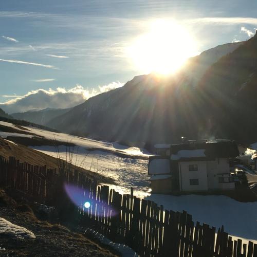 a building with the sun shining on a mountain at Pension Alpenrose in Sankt Sigmund im Sellrain