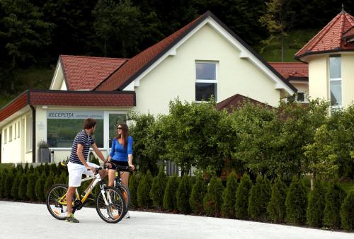 a man and woman riding a bike in front of a house at Apartments & Wellness Skok in Mozirje