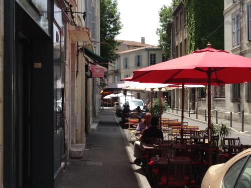 Un groupe de personnes assises à des tables sous un parapluie rouge dans l'établissement Cœur de Provence GP, à Avignon