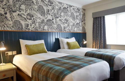 um quarto de hotel com duas camas e um papel de parede em Dartbridge Inn by Greene King Inns em Buckfastleigh