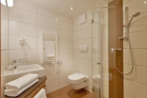 a bathroom with a shower and a toilet and a sink at Hotel Gasthof Jäger Zillertal in Schlitters