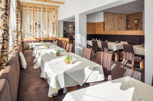 ein Restaurant mit weißen Tischen, Stühlen und Fenstern in der Unterkunft Hotel Garni Panorama in Serfaus