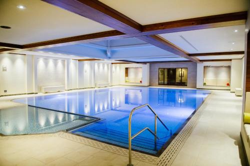 a large swimming pool with blue water in a building at Kettering Park Hotel and Spa in Kettering