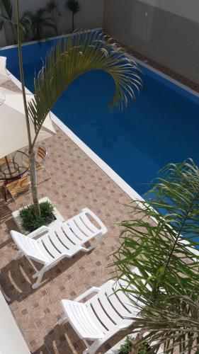 two white lounge chairs and a palm tree next to a pool at Sol de Paracas Apart Hotel Pisco in Pisco