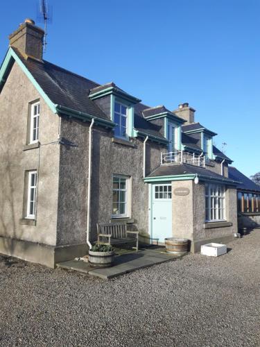 Una gran casa de ladrillo con un banco delante de ella. en Auchencairn Cottage, en Brora