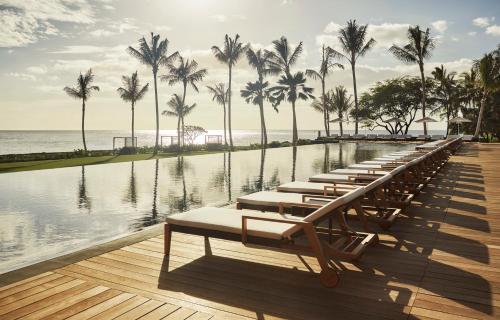 a row of chaise lounges next to a pool with palm trees at Four Seasons Resort Oahu at Ko Olina in Kapolei