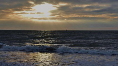 a sunset over the ocean with a lighthouse in the distance at Resort Land & Zee in Scharendijke