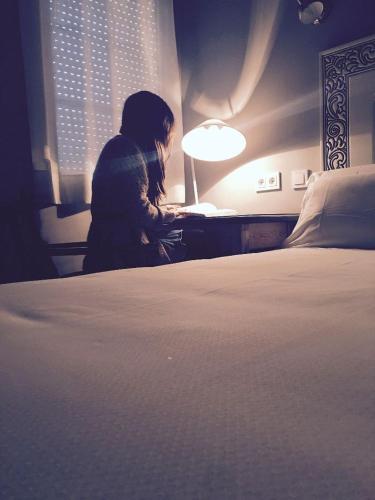 a woman sitting at a desk next to a bed at Hostal Los Castañuelos in Candeleda