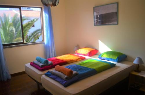 a bed with colorful pillows in a room with a window at Surf House Peniche in Baleal