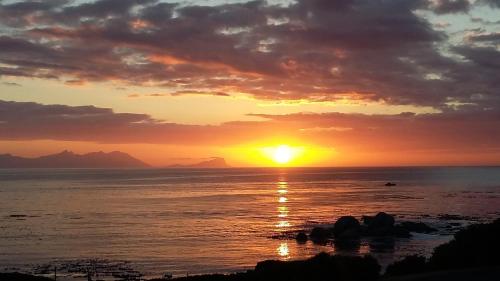 a sunset over the ocean with mountains in the background at Quarterdeck Holiday Apartment in Simonʼs Town