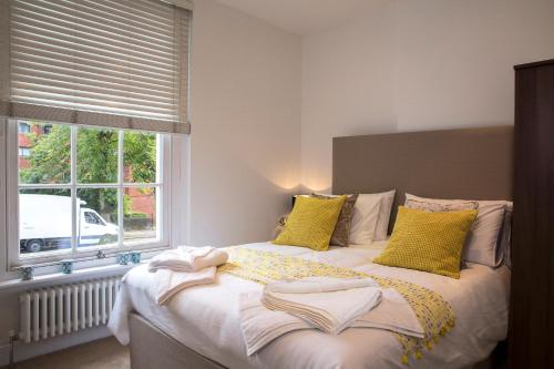 a bedroom with a bed with yellow pillows and a window at Finchley Central Luxury 3 bed triplex loft style apartment in Hendon