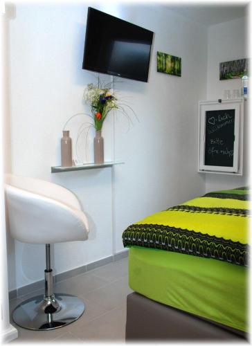 a bedroom with a bed and a chair and a tv at Gästehaus Bacchus in Wachenheim an der Weinstraße