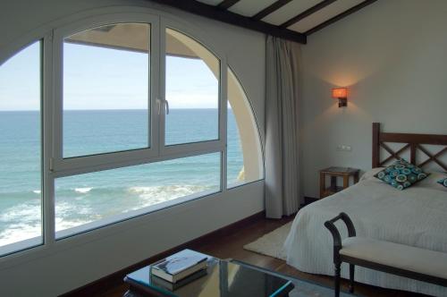 a bedroom with a large window overlooking the ocean at Saiaz Getaria Hotela in Getaria