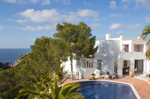 uma grande casa branca com piscina e oceano em Hotel Village em Cala Vadella
