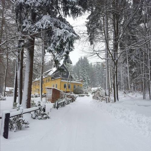 a snow covered yard with a yellow house in the background at Thüringer Waldbaude in Tambach-Dietharz
