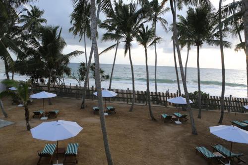 a beach with chairs and umbrellas and the ocean at Oasis Ayurveda Beach Hotel in Ambalangoda