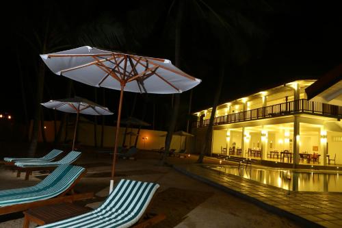 two lounge chairs and an umbrella next to a building at Oasis Ayurveda Beach Hotel in Ambalangoda
