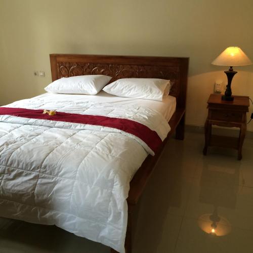a large bed with white sheets and pillows and a lamp at Bagus Homestay in Ubud