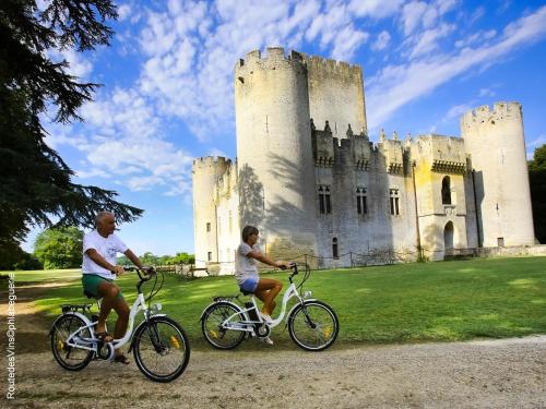 two people riding bikes in front of a castle at La Sauternaise, luxury Boutique B&B in Sauternes