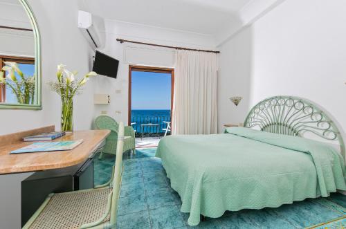 a bedroom with a bed and a desk and a view of the ocean at Hotel Pupetto in Positano