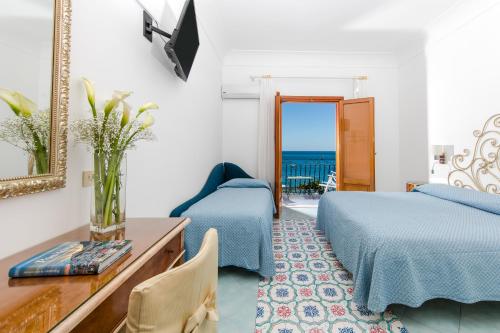 a bedroom with two beds and a table and a mirror at Hotel Pupetto in Positano