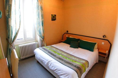 a bedroom with a bed with green pillows and a window at Hôtel Gambetta in Lons-le-Saunier