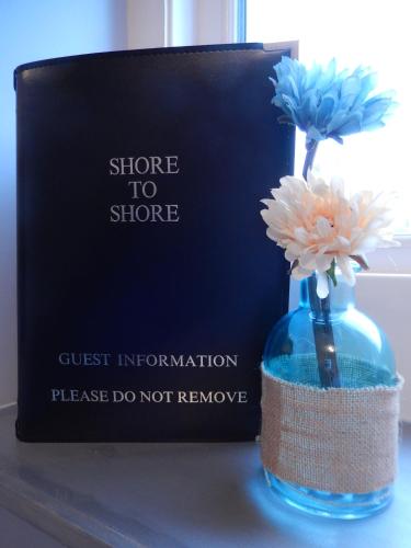 a blue vase with flowers in it next to a book at Shore to Shore in Llandudno