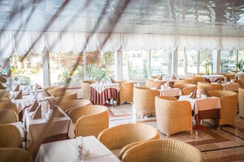 un ristorante con tavoli e sedie bianchi e finestre di Park Hotel a Lignano Sabbiadoro