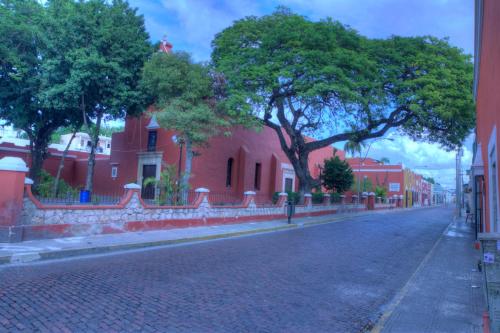 an empty street with a red building and trees at Hotel Luz en Yucatan in Mérida