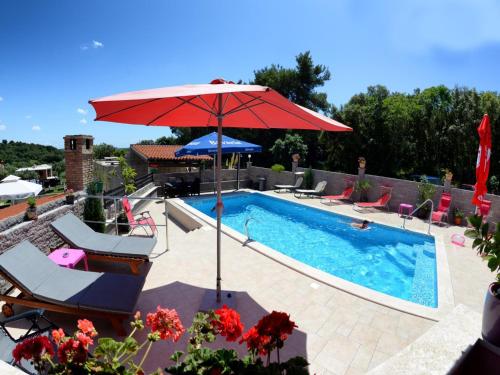 a swimming pool with a red umbrella and chairs next to a swimming pool at Apartments Anita in Pula