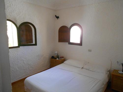 a bedroom with a white bed and two windows at Casa a Calacreta in Lampedusa