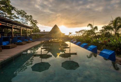 a pool at a resort with a sunset in the background at Nayara Springs - Adults Only in Fortuna