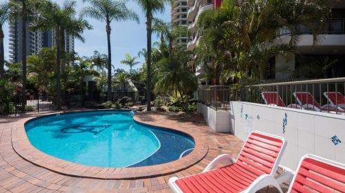 una piscina con 2 sillas de césped y un visor rojo en Alexander Holiday Apartments, en Gold Coast