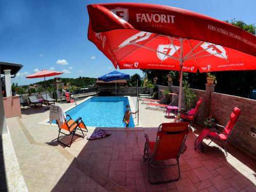 a child is standing by a swimming pool with a red umbrella at Apartments Anita in Pula